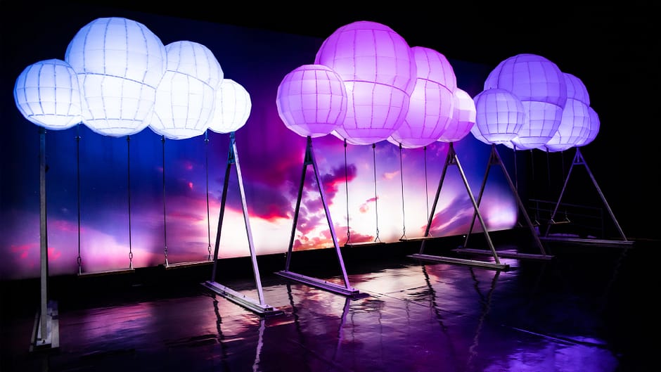 Three swing sets topped with clouds lit up in purples and blues
