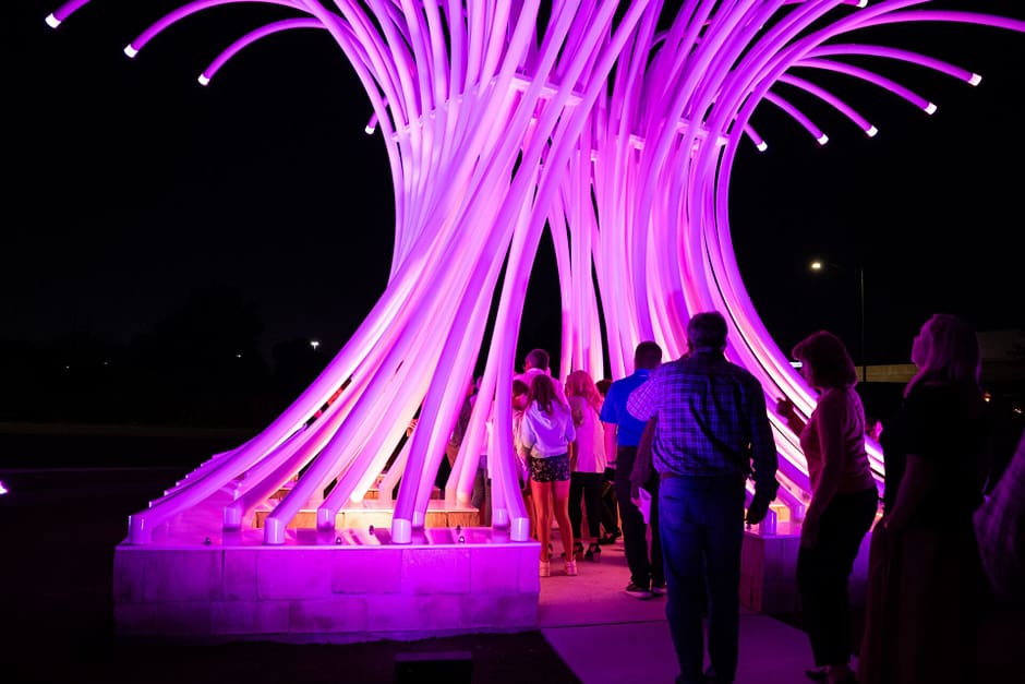 Art installation tree made of multiple lit up rods reaching into the sky and curled as people walk through the middle