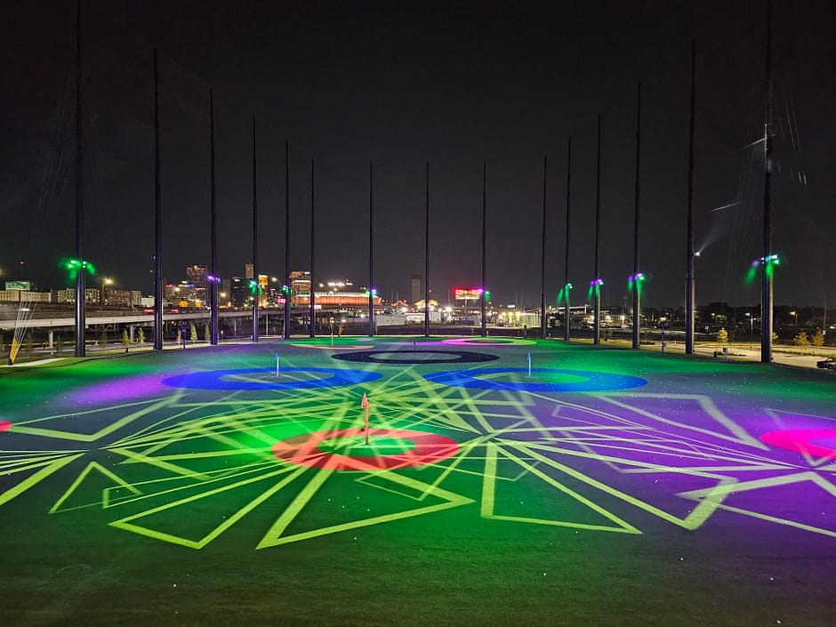 Golf driving range at night with multiple circular and triangular lighting spotlights in various colors