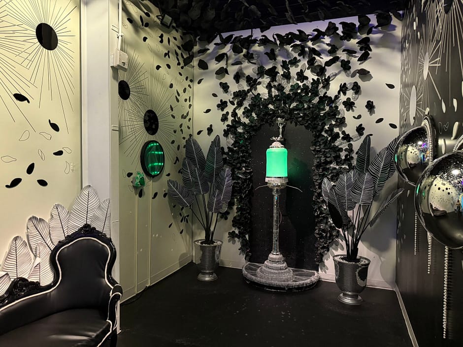 White room with black flowers and art deco designs with a glowing green absinthe dispenser